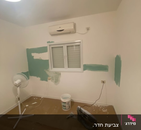 קיר צבוע חלקית בצבע ירוק עם דלי צבע ומברשת